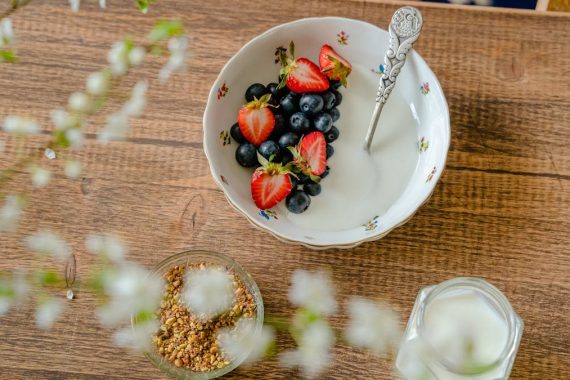 A bowl of fresh strawberries, blueberries with yogurt on a wooden table, viewed from above.