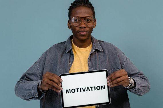 A young African American man holding a tablet displaying the word 'MOTIVATION' against a blue background.